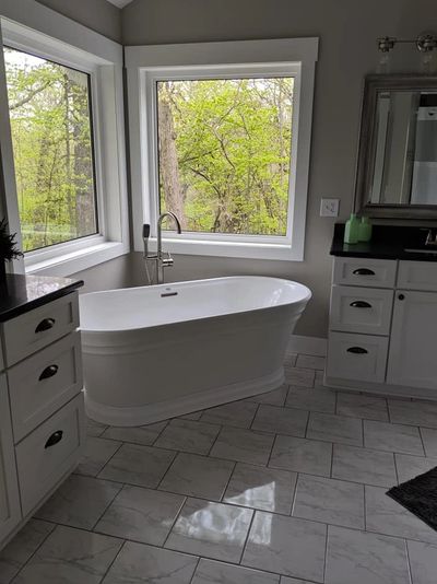 Modern bathroom with a white freestanding bathtub and large windows overlooking greenery.