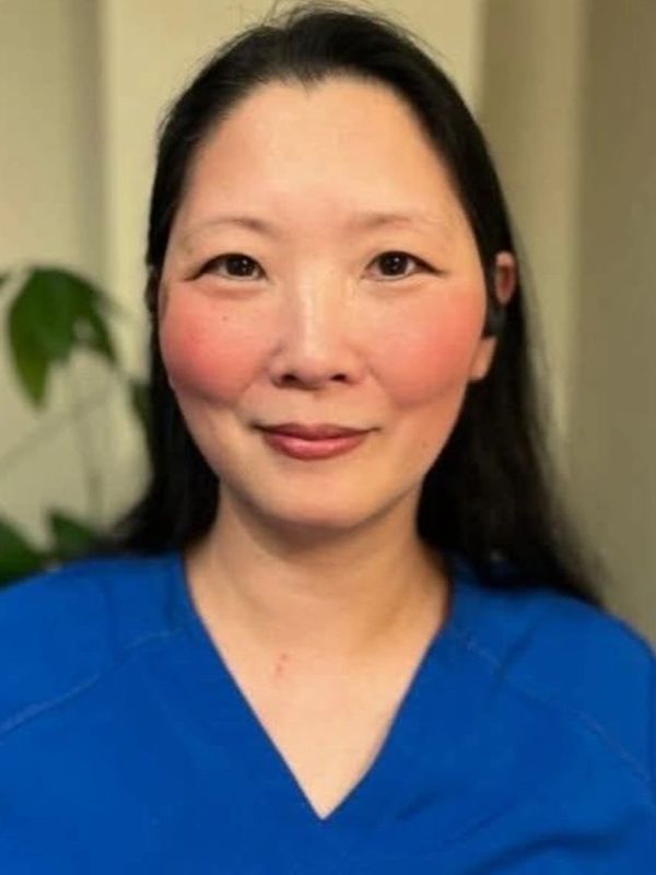Smiling woman in blue scrubs with long black hair.