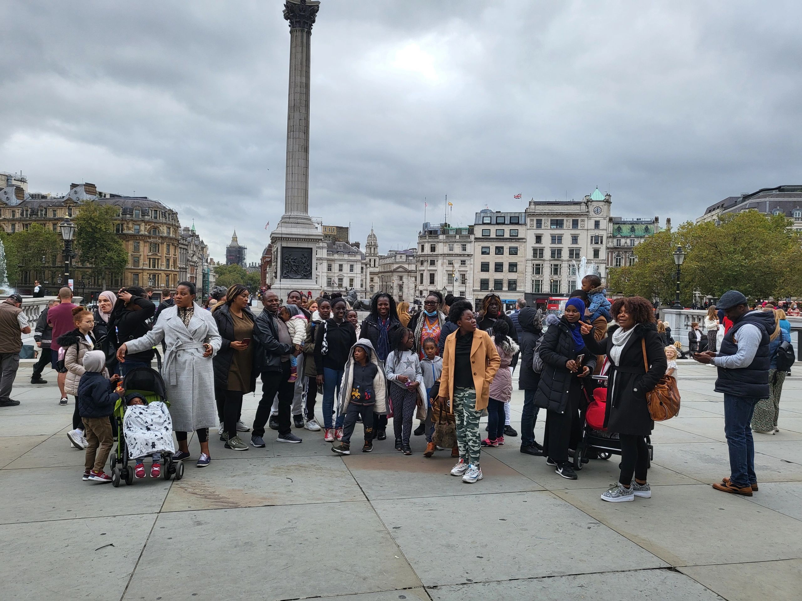 A diverse group of people gathered in a large public square with historical buildings and a tall column.