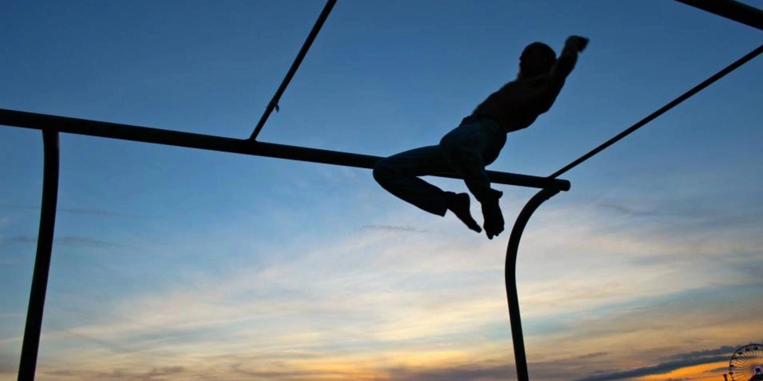 Silhouette of a person swinging on monkey bars at sunset.