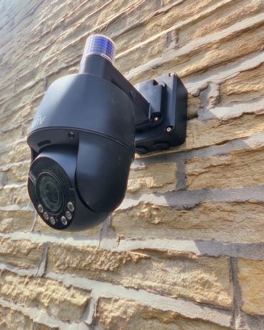 Black security camera mounted on a textured brick wall.