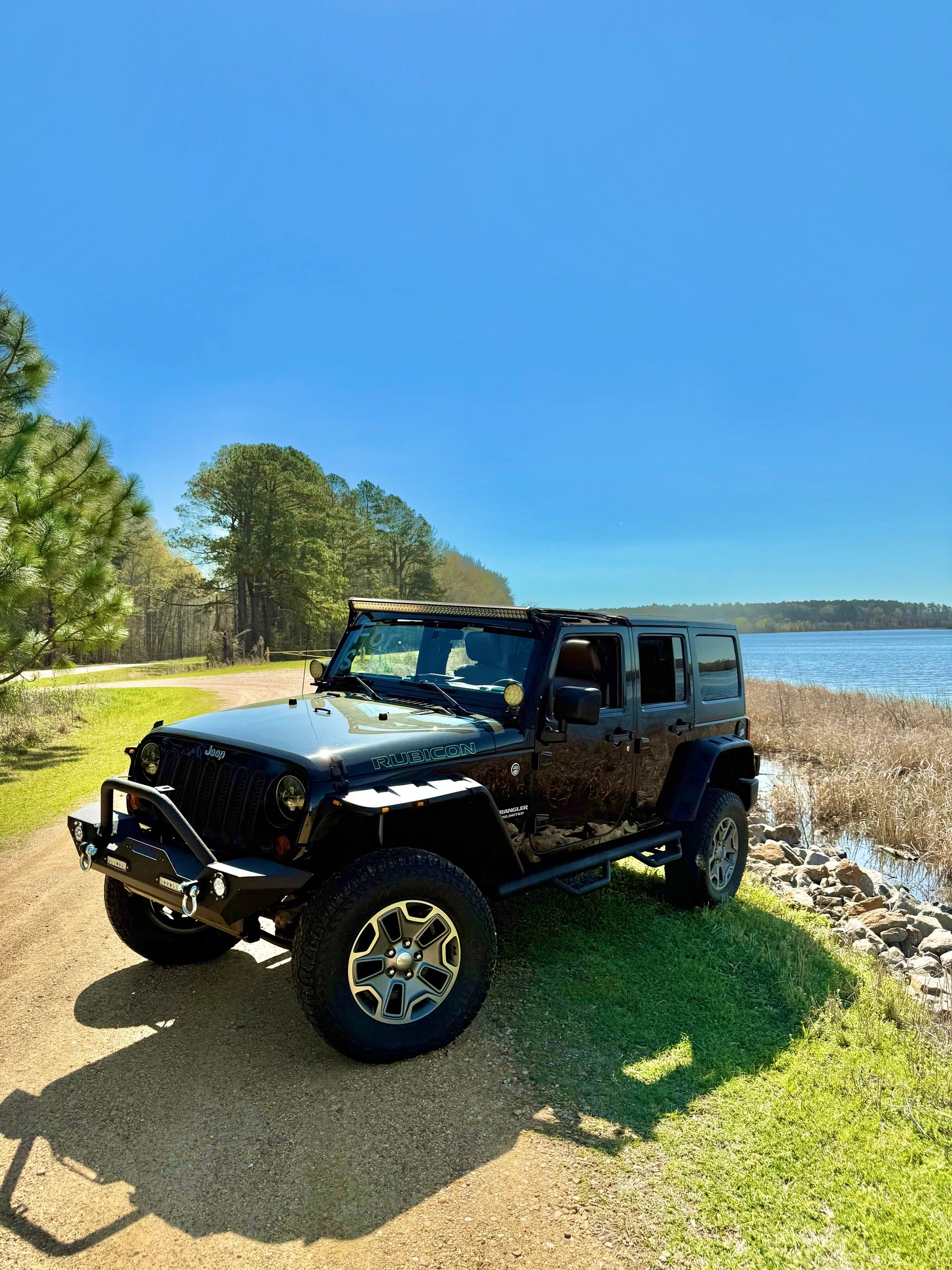 Black Jeep Wrangler Rubicon parked near a lake on a sunny day.