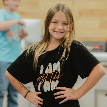 Smiling girl wearing a black t-shirt with the phrase "I am just like I am."