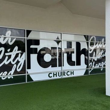 Exterior glass windows of Faith Church with bold white and black lettering.