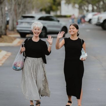 Two women happily waving while walking down a street.