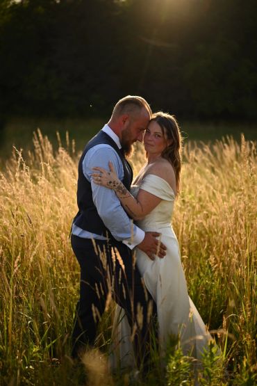 Couple in wedding attire embracing in a sunlit field.