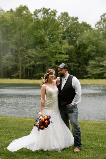 Bride and groom posing near a lake with trees in the background.