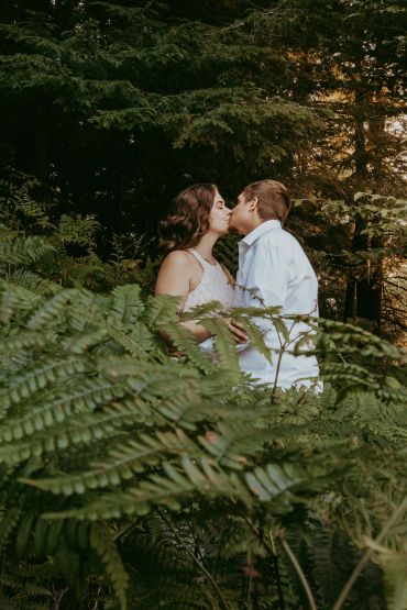 Couple sharing a kiss in a lush forest.
