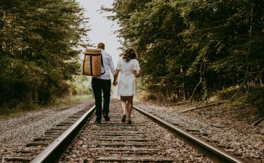 Couple walking hand in hand on railroad tracks.