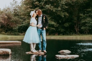 Couple kissing on a rock in the water with trees around.