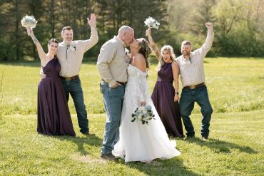 Bride and groom kissing, surrounded by celebrating bridesmaids and groomsmen.