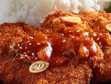 Close-up of crispy fried cutlet with sauce and white rice.
