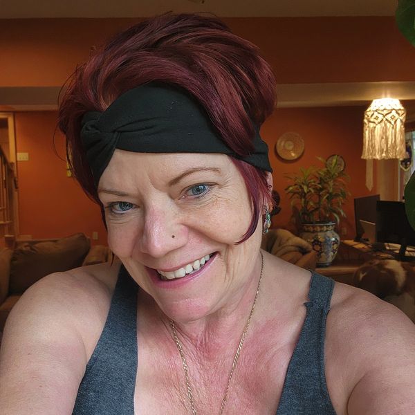 Smiling woman with red hair and a black headband taking a selfie indoors.