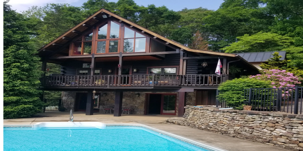 A rustic cabin with a large pool surrounded by trees and flowers.
