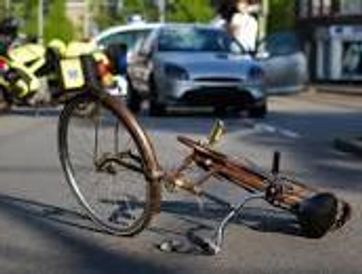 Damaged bicycle lying on the road with a car stopped behind it.