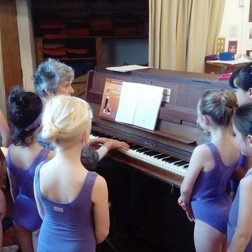 Students gather around the piano. Brewer Dance Academy runs ballet lessons with live music.