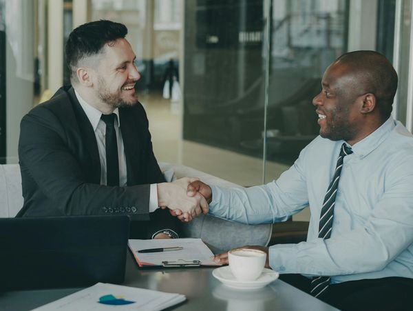 Two hands almost touching amidst tall concrete structures.