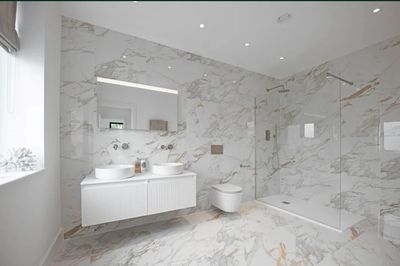 Modern bathroom with white marble walls and floors, dual sinks, and a walk-in shower.