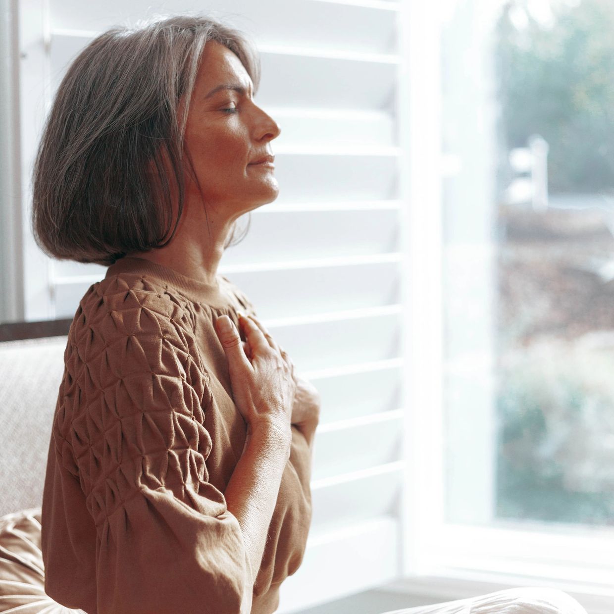 Calm woman meditating indoors with eyes closed and hands on chest.