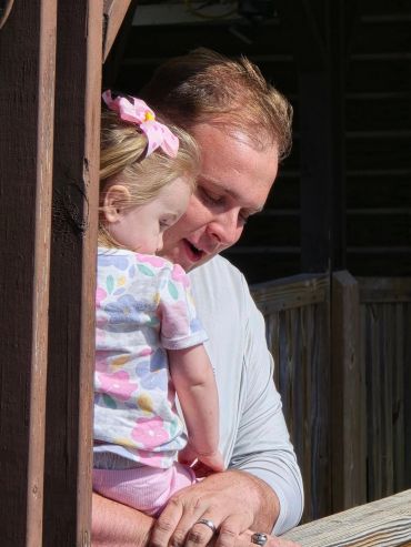A man lovingly holds a young girl with a pink bow in her hair.