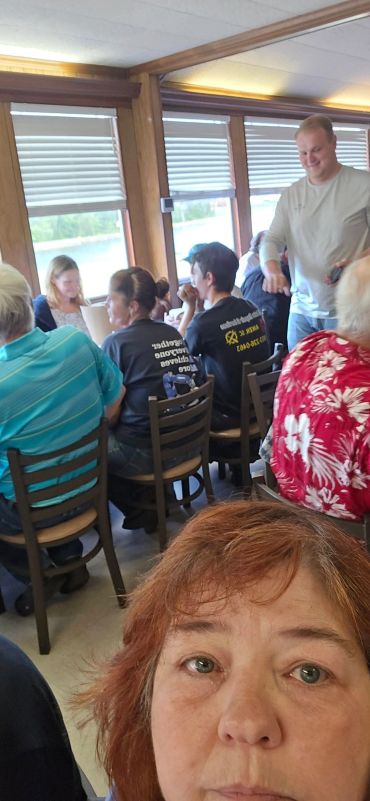 A woman takes a selfie in a crowded room with people seated and chatting.