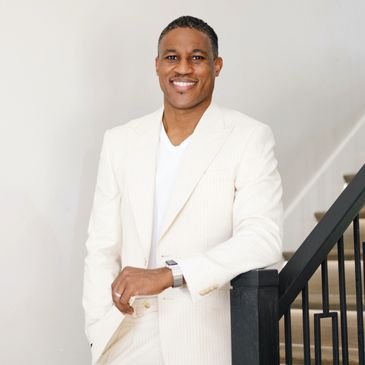Smiling man in a white suit leaning on a railing.