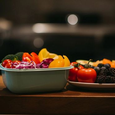 A colorful assortment of fresh vegetables and fruits in containers on a wooden surface.