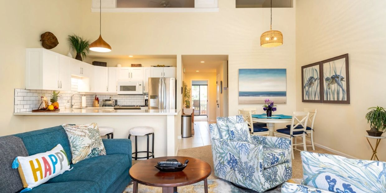 Bright living room with blue sofa, patterned chairs, and open kitchen.