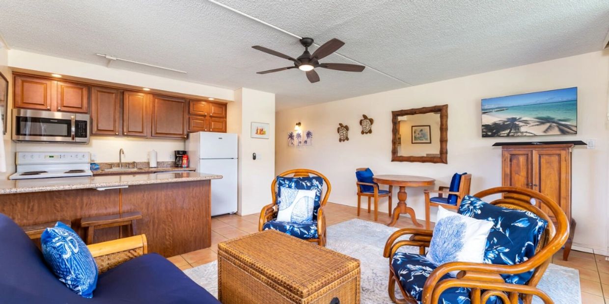 Cozy living room with tropical-themed cushions and wooden furniture beside a compact kitchen.
