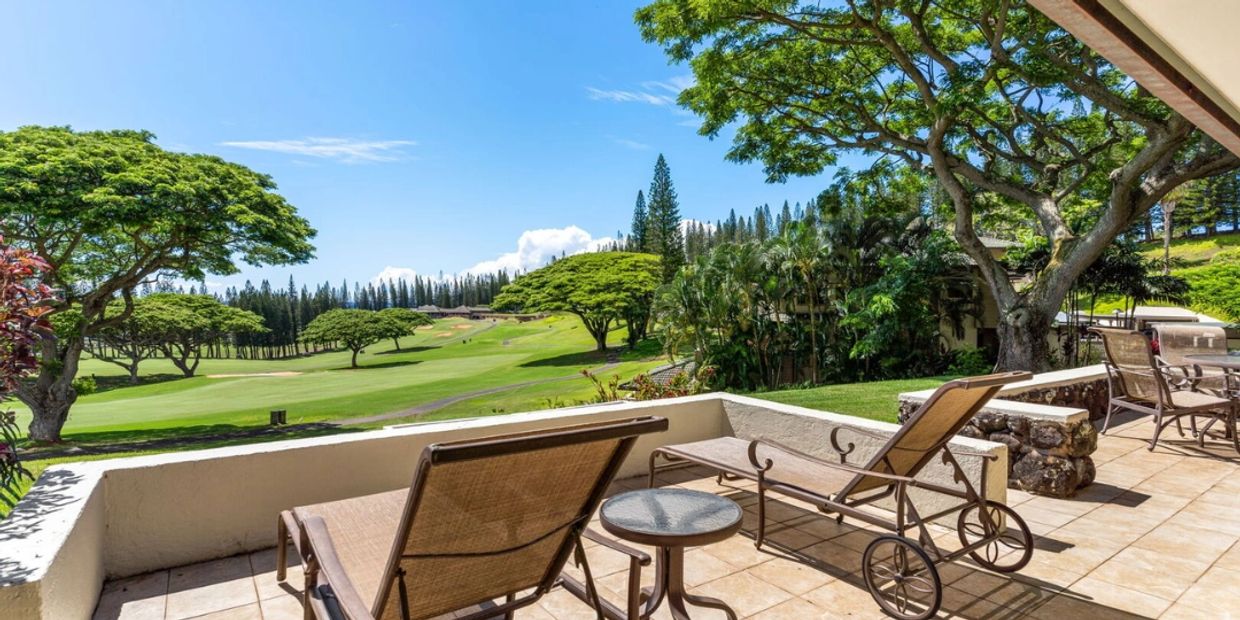Sunny patio with loungers overlooking a lush golf course and trees.