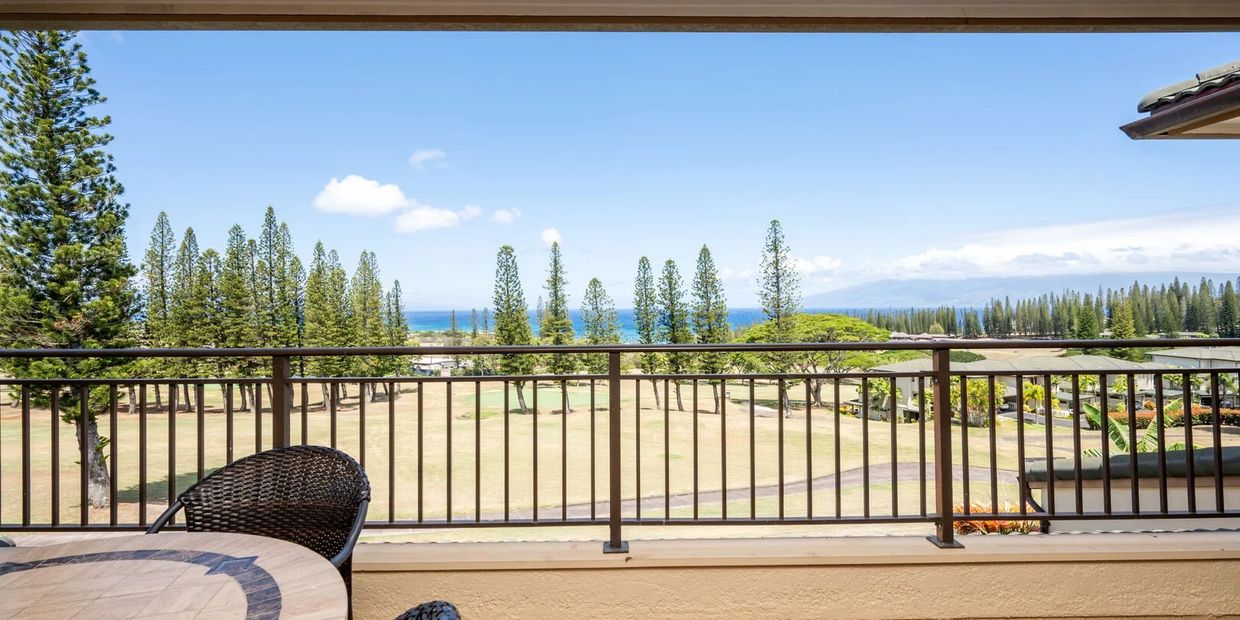 Balcony view overlooking a golf course and ocean with tall pine trees.