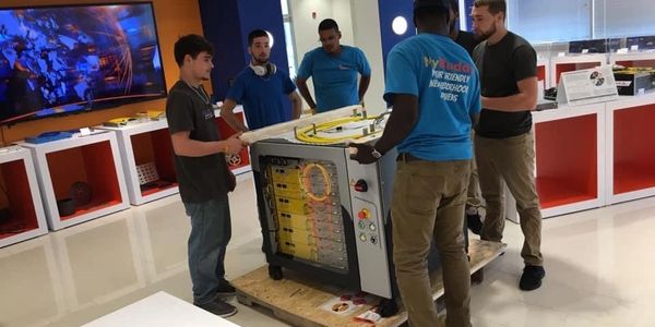 Five men stand around a large electronic device inside a modern showroom or office space.