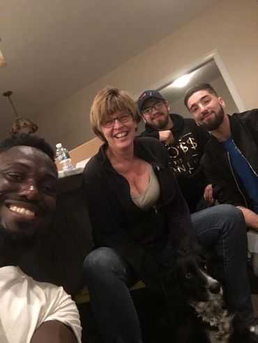 Four friends smiling indoors with a black and white dog.