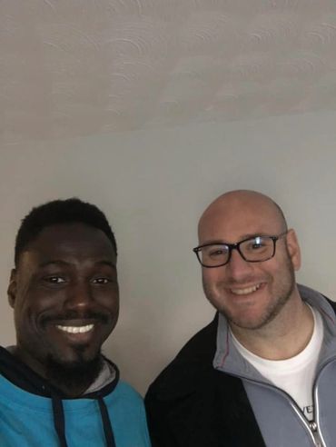 Two men smiling for a friendly selfie indoors.