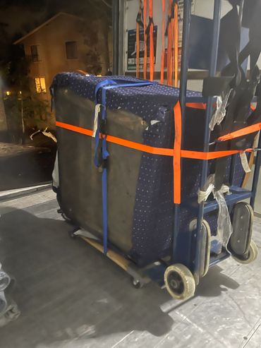A large wrapped item secured with orange and blue straps on a dolly at night.