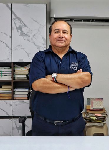 Man in navy blue shirt stands confidently with arms crossed in an office.
