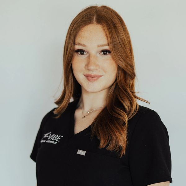 Smiling woman with red hair wearing a black VIBE scrub top.