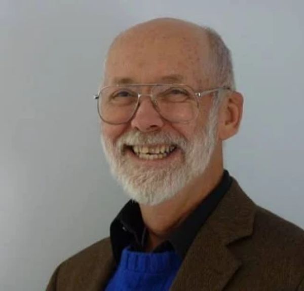 Smiling elderly man with glasses and white beard.