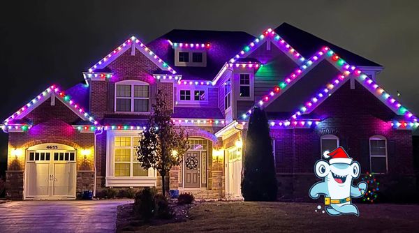 A large house decorated with colorful Christmas lights and a Santa-themed cartoon character.