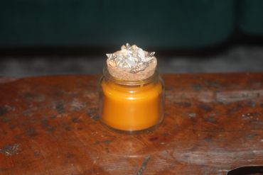 A jar candle with a cork lid decorated with tiny seashells.