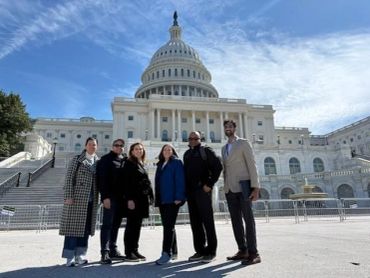 Group of six people standing in front of the U.S. Capitol building.