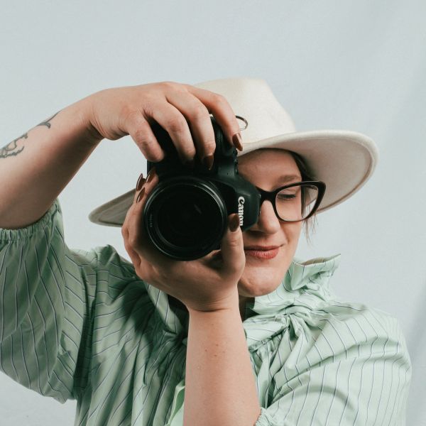 Person wearing a hat and glasses taking a photo with a camera.