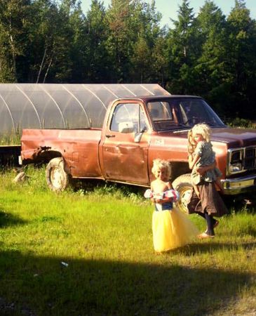 Two children near an old brown pickup truck in a grassy area with trees.