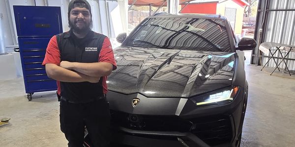 Man standing confidently next to a sleek black Lamborghini inside a garage.