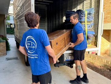 Two movers carrying a wooden cabinet into a truck.