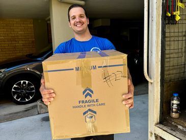 Man holding a large cardboard box labeled fragile, smiling.