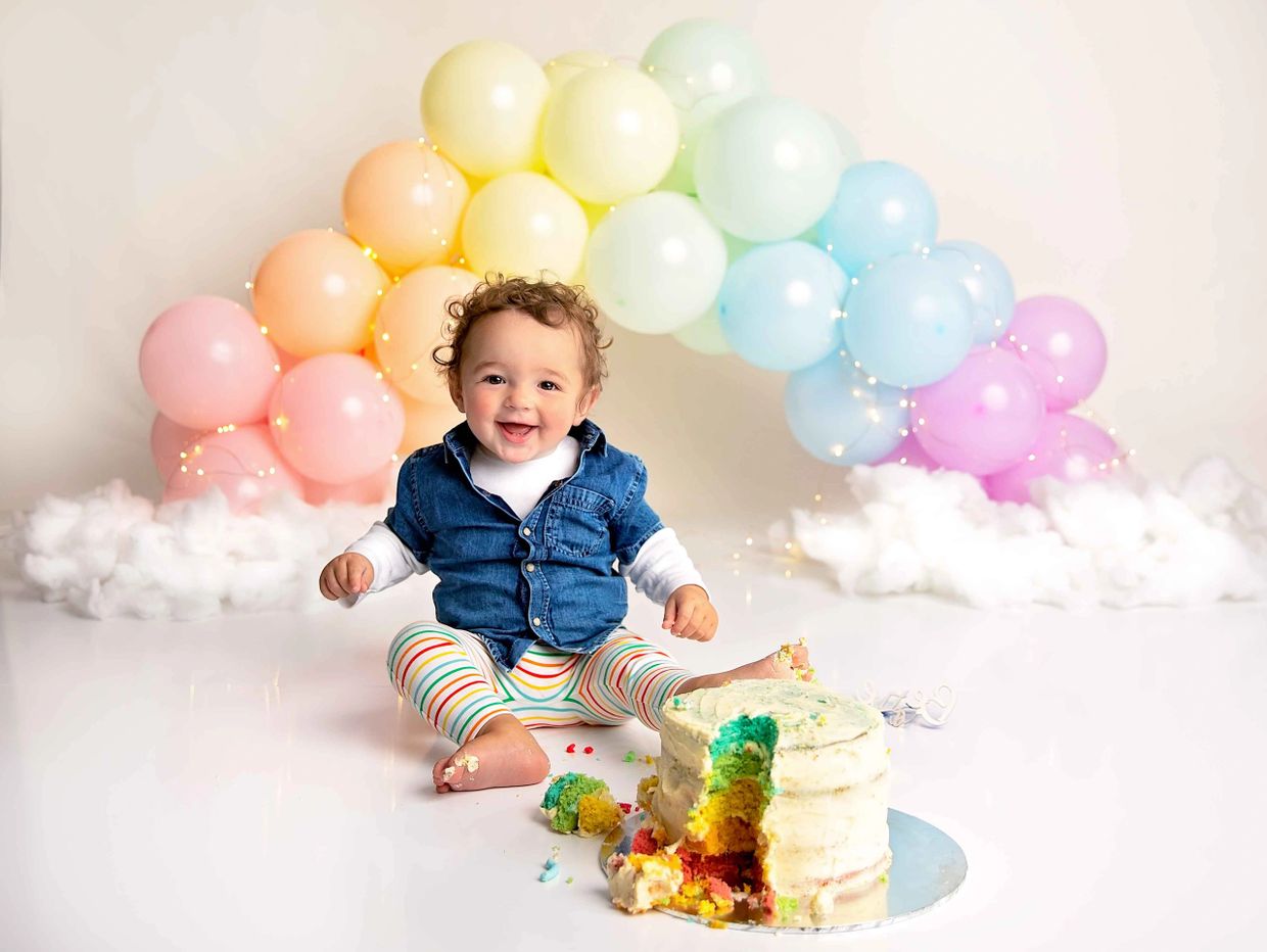 Rainbow balloon arch with rainbow cake, boy wearing a denim shirt and stripe leggings.