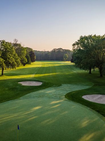 Sunlit golf course with green fairways and sand bunkers.