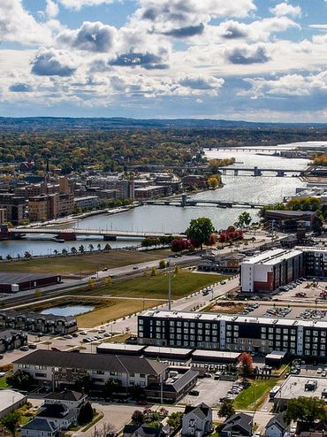 Aerial view of a cityscape with river, industrial area, and residential neighborhood under a partly cloudy sky.