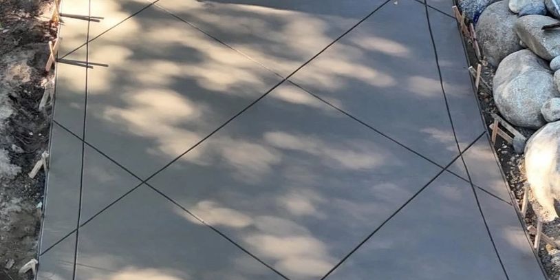 Newly poured concrete driveway with decorative joint lines and a person sitting on rocks.